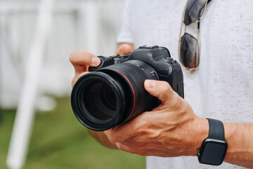 dslr camera in hands, young adult caucasian photographer in white t-shirt at work outdoors in sunny summer day