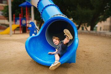 Happy Child Playing on Blue Slide in Playground