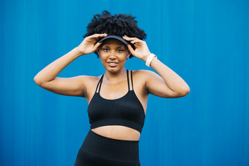 Portrait of a young cheerful woman standing against a blue background, making a break during her workout session.