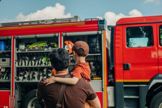 Father carrying son in front of fire truck