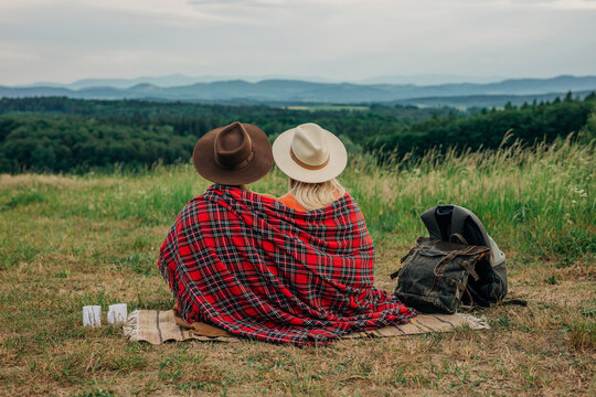 Young couple wearing hat and plaid shawl sitting on meadow at mountain