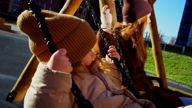 Mother And Daughter Swinging On Playground In Spring