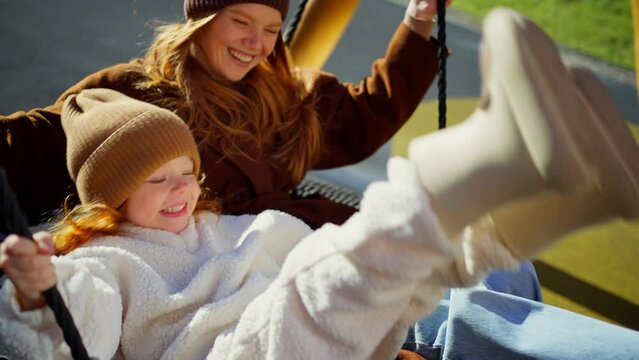 Mother And Daughter Swinging On Playground In Spring