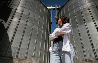 Confident worker standing in front of industrial silos under clear blue sky