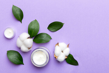 Organic cosmetic products with cotton flower and green leaves on color background. Copy space, flat lay