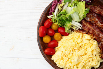 Breakfast plate . Scrambled eggs , bacon , cherry tomatoes and salad
