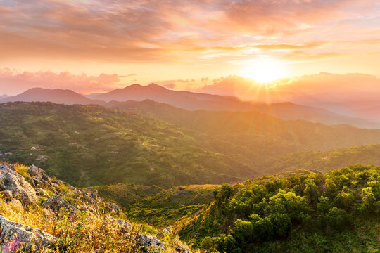 highland mountain landscape of beautiful sunset or sunrise with nice mountain peaks and slopes, green and golden hills and majestic cloudy sky on background