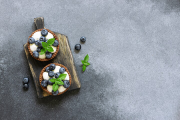 Fresh homemade tart with cream, blueberries and basil leaves on dark stone background with copy space for your design. Food blog or cook book cover concept.