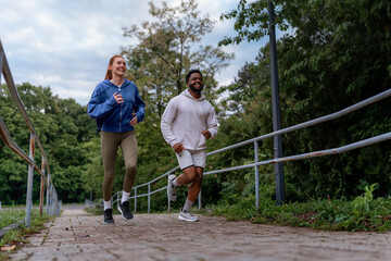 Man and woman jogging up a hill on a paved path, laughing and enjoying their run together. They are dressed in hoodies and athletic leggings.