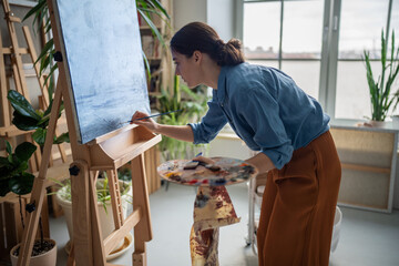 Focused female artist working out details of painting, working with small paintbrush, applying...