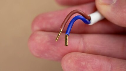 Stripped and ready to connect electrical wires with copper tips in the hand of an engineer on a brown background