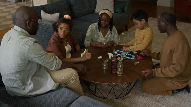 Full shot of multigenerational African American family having fun together. Mother, father and daughter playing domino and arguing about rules, while little boy is playing board game with granddad