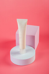 Plastic white tube for cream or lotion. Skin care or sunscreen cosmetic with stylish props on pink background.