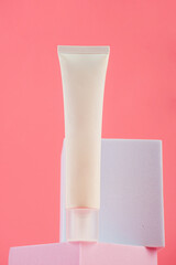 Plastic white tube for cream or lotion. Skin care or sunscreen cosmetic with stylish props on pink background.