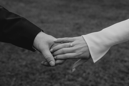 close up of the hands of bride and groom holding each other, showing the engagement ring in black and white