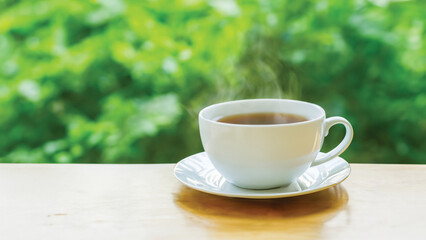 coffee cup in around coffee beans on Wooden tabletop with blurred tea plantation landscape against blue sky and blurred green leaf frame Product display concept natural background