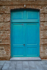 blue painted Wooden door gate in red brick stone arch. Old, vintage wood arched door in red brick wall. house home vintage retro aged exterior. grey tiled floor. front view. lantern aboму doorway