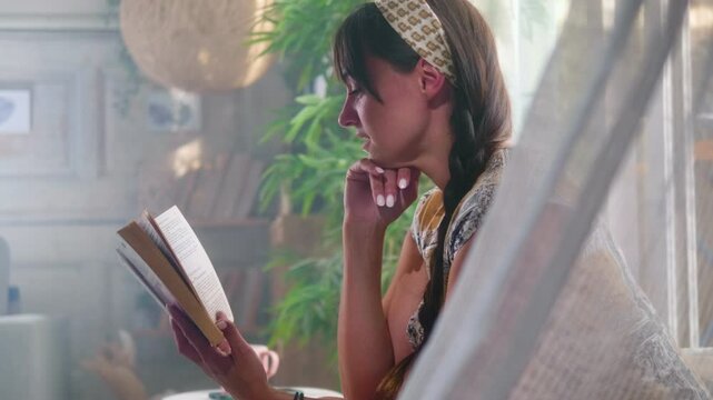 Smiling 30s woman enjoys reading book in free time in boho interior at home