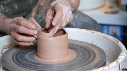 Hand shaping clay pottery with a tools at throwing wheel.