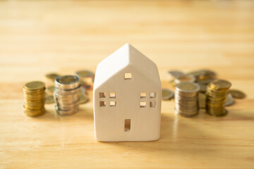A house model and coins are placed on a wooden table with copy space. Concepts of finance, banking, loans and buying-selling or mortgaging real estate.