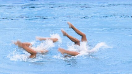 Artistic swimmers team performing synchronized choreographed legs movement in the swimming pool