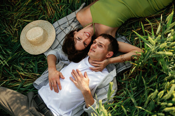 Couple is lying down on the agricultural field with high wheat that is growing