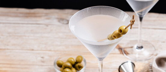 Vodka martini cocktail with vodka and vermouth and green olives on wooden table. Panorama view