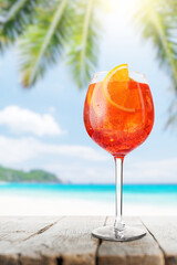Glass of Aperol Spritz on a table with a stunning sea and beach background