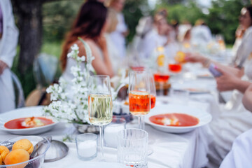 Glasses and plates on a covered festive table with a tablecloth. Gazpacho soup, fruits and alcoholic beverages. Delicious food and snacks at a street party.