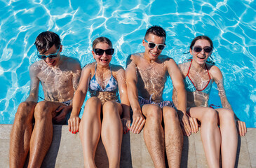 Cute teens friends in swimsuits and sunglasses are laughing in the pool. Smiling boys and girls...