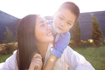 Asian laughing mom and son on a green lawn