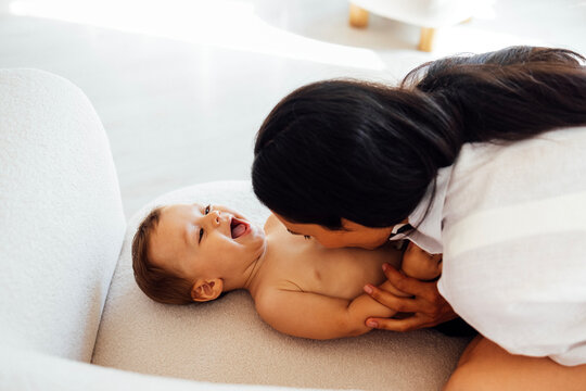 A young woman kisses her laughing baby. An attractive mom is tickling her cute son.