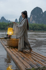 Hanfu Girl holding a lantern on a bamboo raft, Xingping, China. Vertical