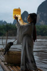 Hanfu Girl holding a lantern on a bamboo raft, Xingping, China. Vertical