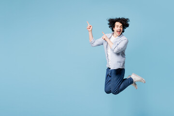 Full body young man he wear shirt white t-shirt casual clothes jump high point index finger aside on area mockup isolated on plain pastel light blue cyan background studio portrait. Lifestyle concept.