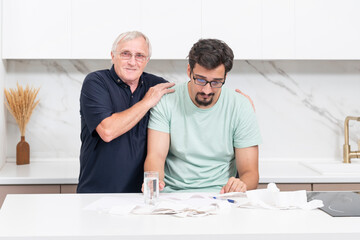 Close up of unhappy man and his elderly father sitting at the table, stressed and confused by...