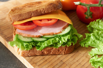 Sandwich with ham, cheese, lettuce and tomato on wooden board