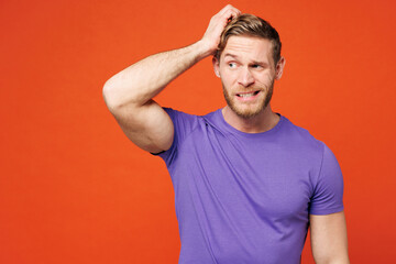 Young sad shocked confused puzzled unhappy man wear purple t-shirt casual clothes look aside hold scratch head look aside on area isolated on red orange background studio portrait. Lifestyle concept.