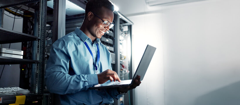 Laptop, server room and black man on network for maintenance, programming software or typing. Tech, data center and happy engineer on system database for information, cybersecurity or cloud computing - Powered by Adobe