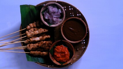 Chicken satay with peanut sauce, chili sauce, and sliced onion, indonesian skewer cuisine, served on wooden plate, isolated white