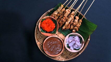 Chicken satay with peanut sauce, chili sauce, and sliced onion, indonesian skewer cuisine, served on wooden plate, isolated white
