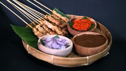 Chicken satay with peanut sauce, chili sauce, and sliced onion, indonesian skewer cuisine, served on wooden plate, isolated white