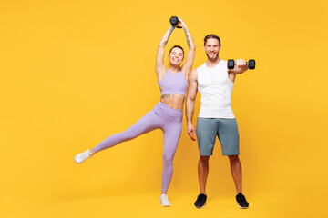 Full body young cheerful strong fitness trainer sporty two man woman wear blue clothes spend time in home gym hold dumbbells look camera isolated on plain yellow background. Workout sport fit concept.