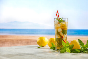 Glass of fresh icy lemonade with mint leaves and lemons on wooden  table. Copy space for drinks and food and products. Seascape in summer background.