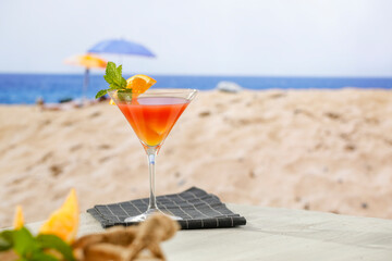 Cool fruit cocktail. Drink on white wooden board table top and blur background of a beach and a seascape. Advertising space empty for products.
