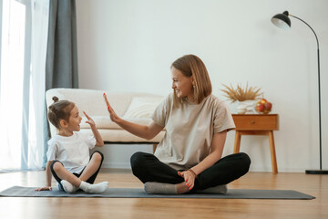 Smiling, positive facial expression. Young woman with little girl are doing yoga at home