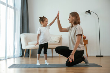 Well done, doing high five. Young woman with little girl are doing yoga at home © standret