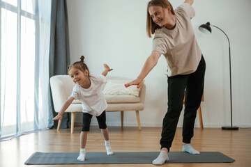 Focused on the exercise. Young woman with little girl are doing yoga at home