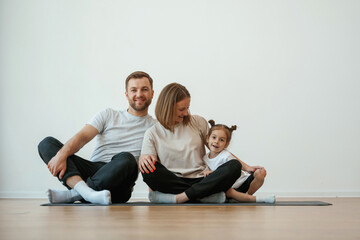 Obraz premium Cheerful people. Family of mother, father and daughter are doing yoga at home