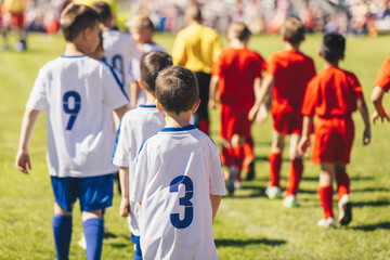 Fototapeta premium Boys in football shirts enter the field in two rows. Kids play school soccer tournament. Children compete in two football teams outdoors